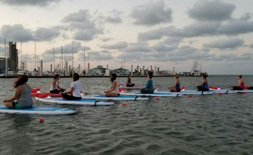 Water Dog, a new yoga studio, opened in mid-June on Corpus Christi Bay. Headquartered in a houseboat at the Corpus Christi Marina, Water Dog offers classes in yoga, pilates and core strengthening on deck and in the water on paddleboards. Here, a class practices yoga during a full moon on the bay. Courtesy photo