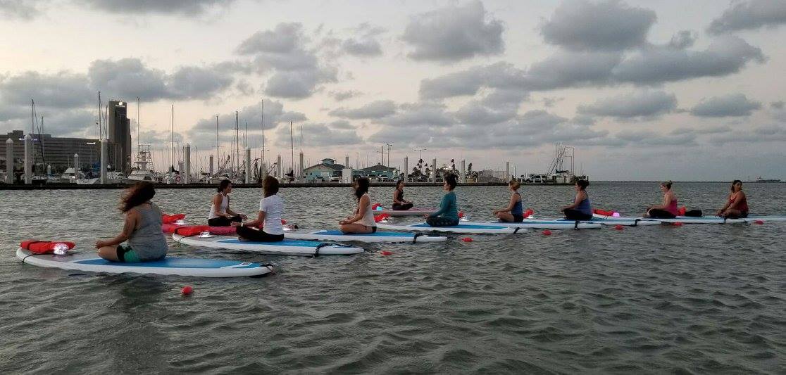 Water Dog, a new yoga studio, opened in mid-June on Corpus Christi Bay. Headquartered in a houseboat at the Corpus Christi Marina, Water Dog offers classes in yoga, pilates and core strengthening on deck and in the water on paddleboards. Here, a class practices yoga during a full moon on the bay. Courtesy photo