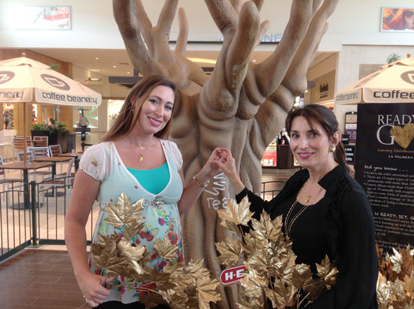 Jessica Hester (left) and Barbara Canales in front of the gold tree representing the Ready. Set. Gold campaign to raise awareness of pediatric cancer. The pair, who both have daughters who have suffered from cancer, hope to fill the tree with gold leaves. Each leaf represents $1 raised in the campaign. Photo by Suzanne Freeman