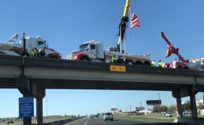 Firefighters hoist an American flag on an overpass in Corpus Christi in honor of fallen police officer Alan McCollum as a procession accompanying the officer’s hearse makes it way to Church Unlimited for the funeral February 6. Photo by Amber Weems